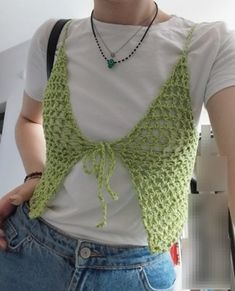 a woman wearing a white t - shirt with a green crochet top on