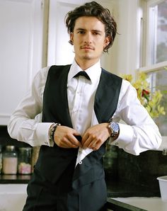 a man wearing a black vest and white shirt is standing in front of a counter