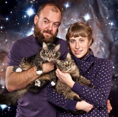 a man and woman holding two cats in front of the camera with stars behind them