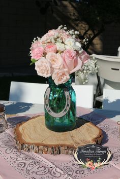 a green vase filled with pink and white flowers sitting on top of a wooden slice