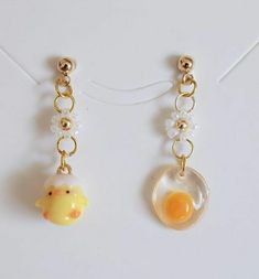 two earrings with charms attached to them on a white surface and one has an egg in the middle