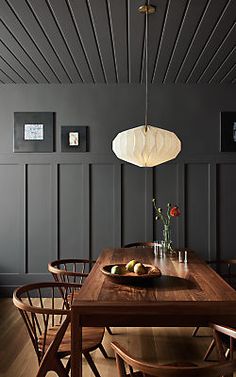 a dining room table with chairs and a bowl of fruit on it in front of dark wood paneling