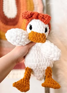 a crocheted white and orange duck with black eyes is held up to the camera