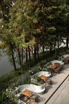 tables and chairs are lined up along the water's edge with trees in the background