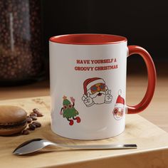 a red and white coffee mug sitting on top of a wooden table next to a spoon