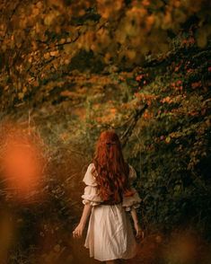 a woman with long red hair walking through a forest in the fall, looking back