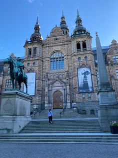 a person standing in front of a large building with stairs leading up to the entrance