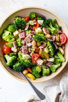 a bowl filled with broccoli, tomatoes and other vegetables next to a fork