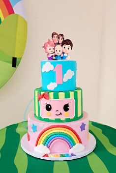 a three tiered cake decorated with cartoon characters and rainbows on the top layer