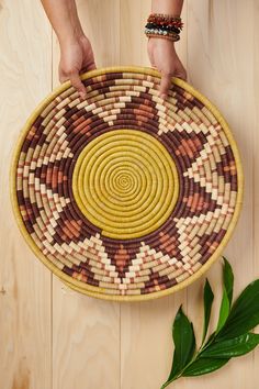 a person holding a woven basket on top of a wooden floor next to a plant