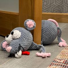 a crocheted mouse laying on the ground next to a wooden post and rug