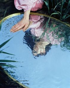 a person's feet sticking out of the water in front of grass and plants