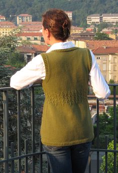 a woman standing on top of a balcony next to a tree filled hillside with houses in the background