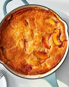 a peach cobbler in a blue cast iron skillet on a white table with plates and utensils