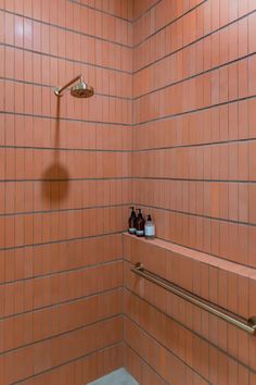 an orange tiled shower with gold fixtures and soap bottles on the shelf next to it