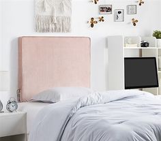 a bed with a pink headboard and white sheets in front of a computer desk