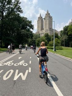 people are riding bicycles down the street in front of tall buildings on a sunny day