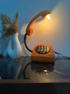 an orange telephone sitting on top of a table next to a vase with a plant