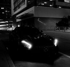 a black sports car parked in front of a building at night with its headlights on