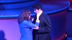 a man and woman standing next to each other in front of a blue stage background