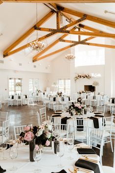 a room filled with tables and chairs covered in white linens, black napkins and flowers