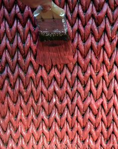 a person with a brush on top of a red woven material wall that is being used as a backdrop