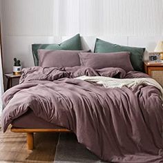 an unmade bed with purple sheets and pillows