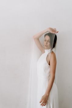 a woman in a white dress is holding her veil over her head and posing for the camera