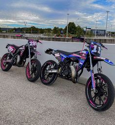 two dirt bikes parked next to each other on top of a parking lot in front of a white wall