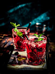 two glasses filled with red liquid and garnished with green leaves