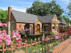 a brick house with pink flowers in front of it and a fence around the yard