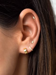 a woman wearing gold ear piercings with two small dots on the side of her ear