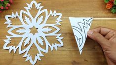 someone is cutting out paper snowflakes on a wooden table with flowers in the background