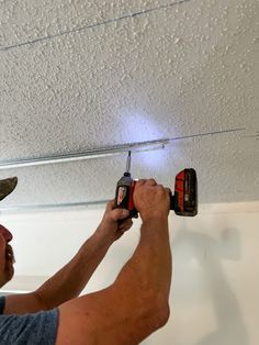 a man is working on the ceiling in his garage while holding two drillers and an electric screwdriver