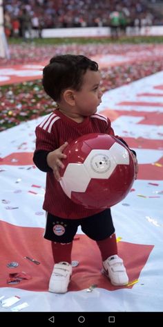 a young boy holding a soccer ball on top of a red and white field covered in confetti