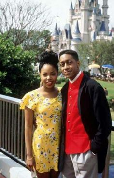 a man and woman standing next to each other in front of a castle at disney world