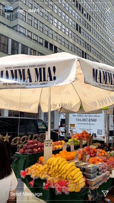 an outdoor market with bananas, oranges and other fruits on display under umbrellas