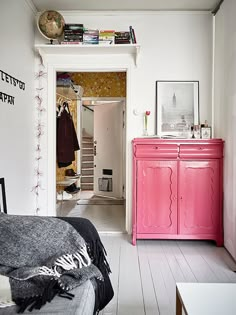 a bedroom with white walls and pink furniture in the foreground, an open door leading to another room