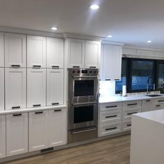 a large kitchen with white cabinets and stainless steel appliances in the center, along with wood flooring