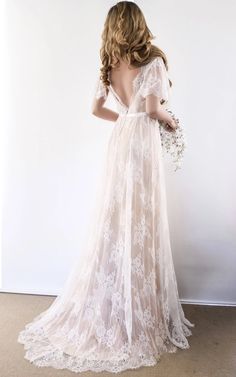 the back of a woman in a white wedding dress standing against a wall with her hands on her hips