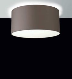 a round light fixture on a black wall with a white ceiling lamp in the background