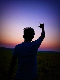 a man standing in a field holding his hand up to the sky