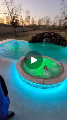 a person standing in front of a pool with blue lights on it and a waterfall