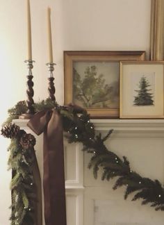 two candles are sitting on top of a mantel decorated with pine cones and greenery