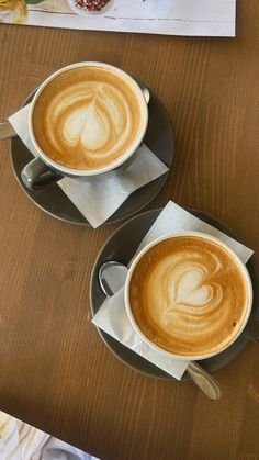 two cups of cappuccino sitting on top of a table next to each other