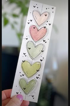 a hand holding up a piece of paper with hearts drawn on it in different colors