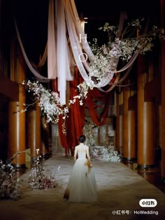 a woman in a white dress is walking down the runway with flowers and ribbons hanging from the ceiling