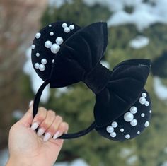 a person is holding up a black minnie mouse ears headband with white pearls on it