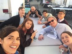 a group of people sitting at a table posing for a photo with their cell phones