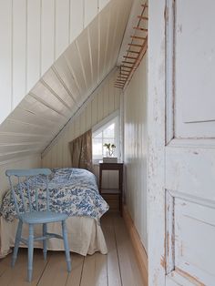 a bed sitting under a window next to a blue chair in a room with white walls